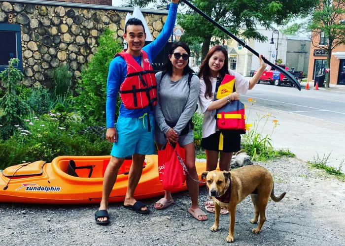 A family with their dog standing next to a kayak 