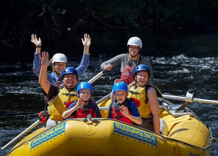 A group of people sitting in white water raft boat and smiling towards the camera