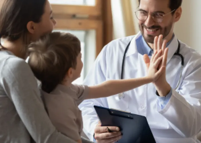A Doctor is giving a high five to a small child. The Doctor is holding a clipboard.