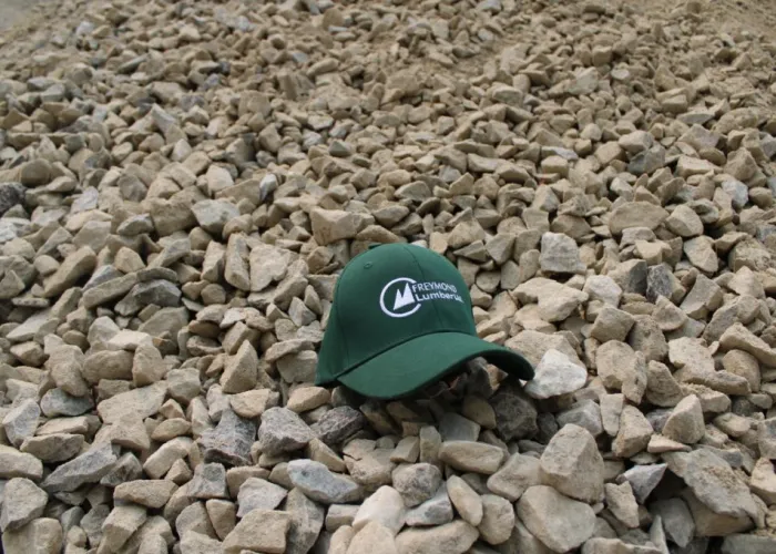 Freymond Lumber. Green hat with Freymond Lumber logo sitting on a pile of stone.