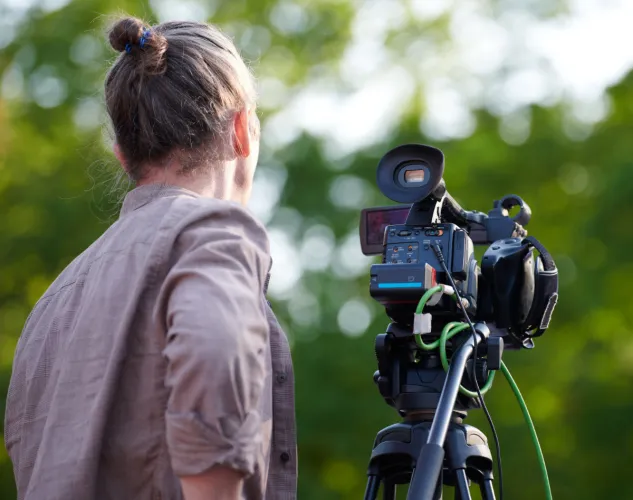 Person with a camera. The image is from the back with trees blurred in the background.